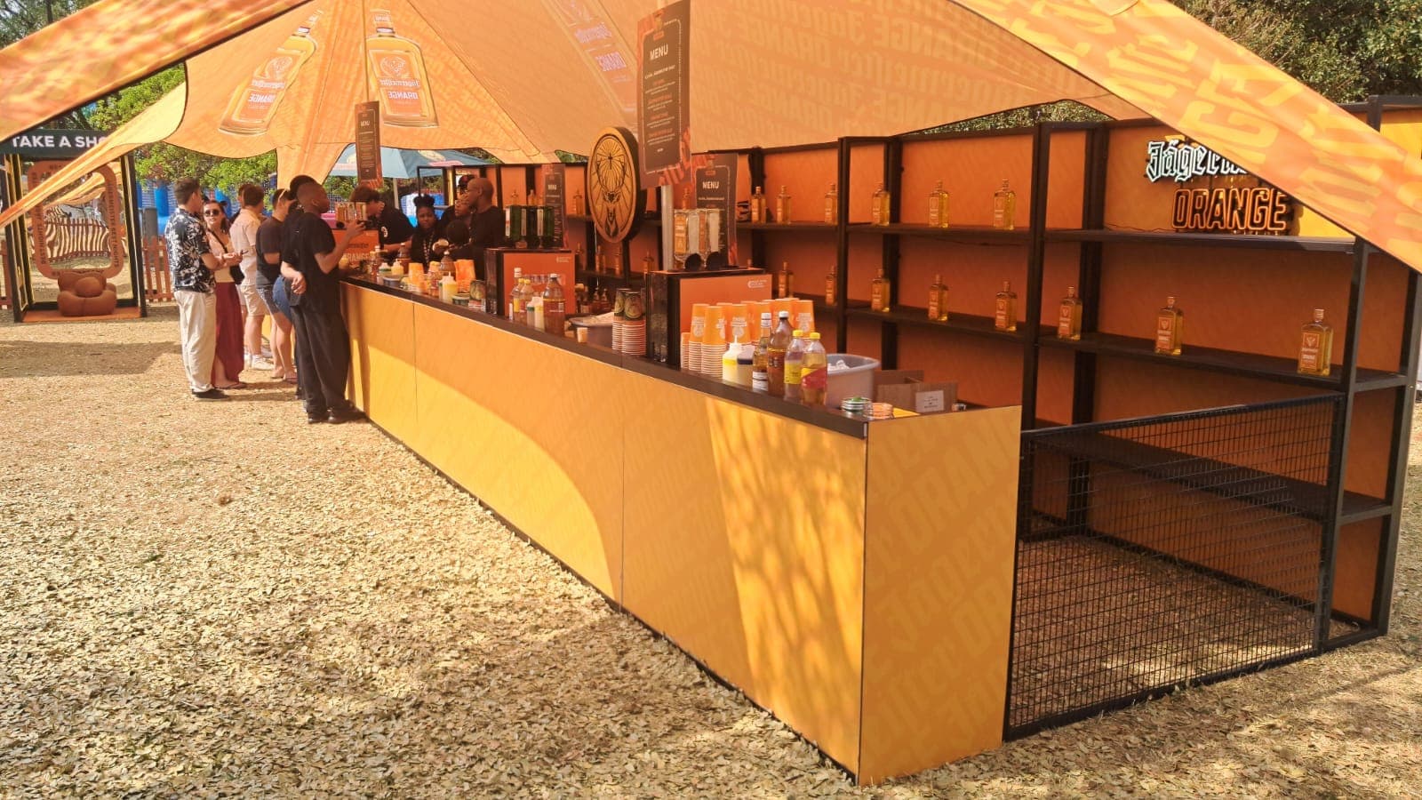 A full-length branded festival bar built by Steady Hand Studios for Jagermeister Orange, staffed and serving a queue of customers